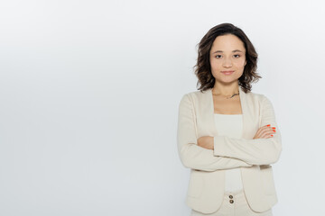 Brunette businesswoman in formal wear crossing arms isolated on grey, feminism concept.