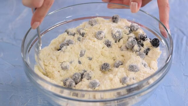 Female hands making blueberry scone dough in glass bowl.