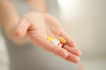 Close-up view of pill in hand. In the background is a pregnant woman. Taking vitamins during...