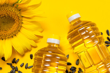 Plastic bottles with sunflower oil, fresh yellow sunflowers, sunflower seeds on yellow background....