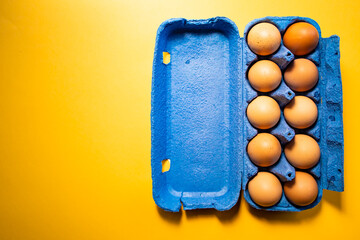 Blue eggs container with ten eggs, on yellow background. Copy space