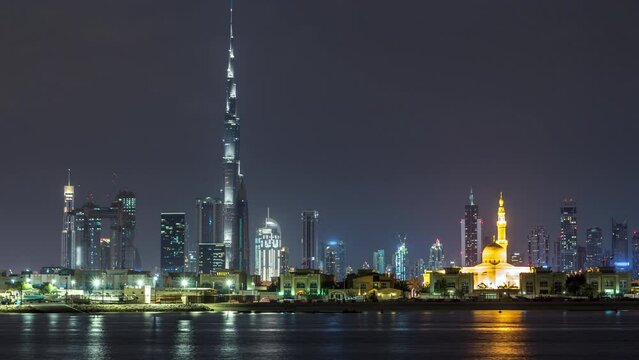 Modern Dubai city skyline timelapse at night with illuminated skyscrapers over water surface
