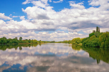 Clouds ans green trees are reflected in water of lake. Beautiful peaceful Ukrainian landscape. Ukraine, Uman, Ostashivskiy lake