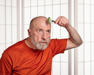 senior man is using a jade stone roller for a face massage, skin care routine concept