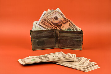 Leather wallet full of cash dollar bills on an orange background. Concept of the importance of saving.