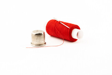 Spool of red thread with a needle and a thimble on a white isolated background.