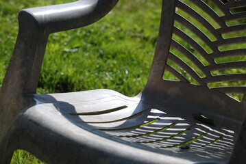 Old white plastic chair. In the garden, on a green lawn, there is a white plastic chair. The paint...