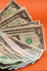 Dollar bills lying on an orange table. Photography in vertical format.