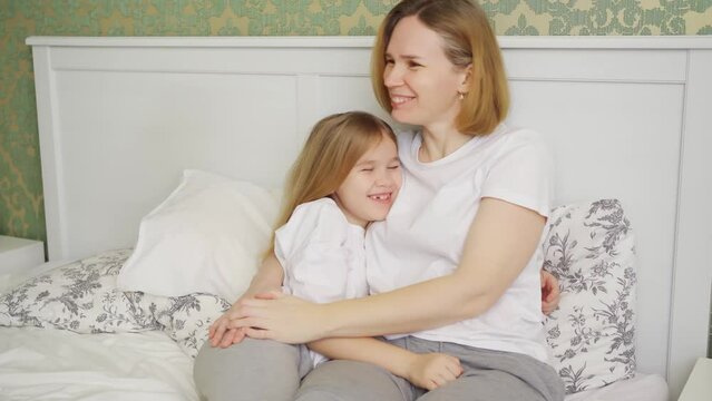 mom and daughter sit in bed having fun, kissing and hugging.
