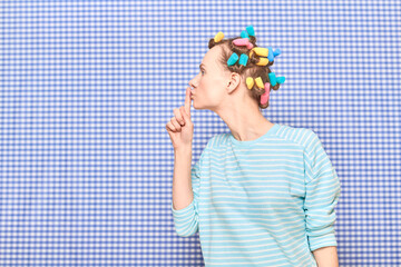 Serious woman with hair curlers on head is showing silence gesture
