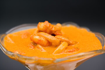 close up shot of shrimp and squid rings in sauce, served in a glass cup, isolated background