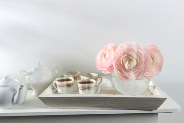Three pale pink ranunculus in a transparent round vase on the white windowsill. Copy space. Place for text