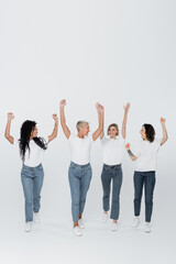 Obraz premium Positive multiethnic women raising hands on grey background, feminism concept.