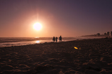familia paseando por la orilla de la playa en la puesta de sol