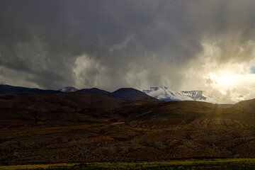 Sun peeks through clouds over snowy hills in Salta, Argentina
