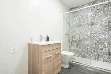bathroom with white porcelain sanitaryware, shower cabin with wall tiled with hydraulic tile and white walls, wooden furniture and dark stoneware floors