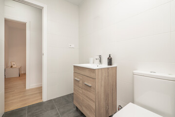 bathroom with white porcelain toilets, white walls, wooden furniture and dark stoneware floors
