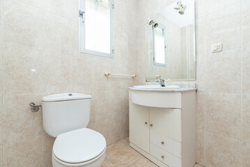 Fototapeta na wymiar bathroom with white porcelain fixtures, cream tile walls, wooden cabinet with marble top and frameless mirror with sconces