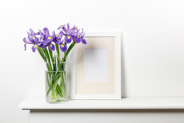 Bouquets of irises in a vase, photo frames on a chest of drawers