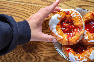 Man's hand holding Cherry filled Danish or Danish bread served in a white plate on a brown wooden...