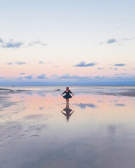 Silhueta de mulher de vestido refletida na àgua durante pôr do sol na praia em Tatuamunha, Alagoas