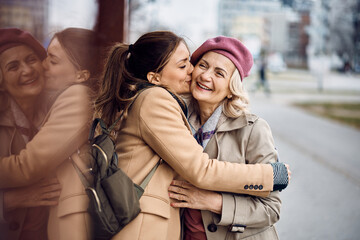 Affectionate woman hugs her senior mother while kissing her on the cheek outdoors.