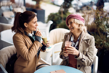 Happy senior woman enjoys in conversation with her daughter while having a drink at sidewalk cafe.
