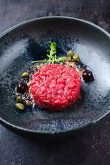Modern style gourmet tartar raw from beef filet with capers and amarena cherry served with truffle cream and lettuce as close-up in a Nordic design plate