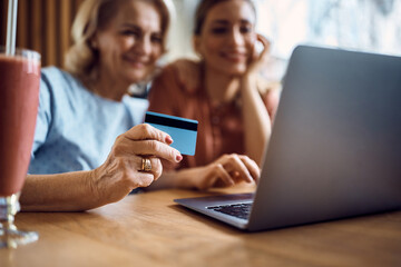 Close-up of senior woman and her daughter using credit card and laptop for online shopping.