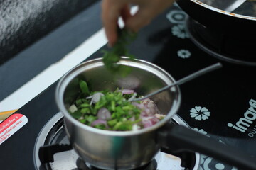 Food being cooked in a stainless steel pot, female hands cooking in a hot pot, stainless steel pot in food on the stove.