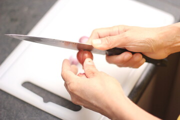 A woman's hand is slicing shallots on a white plastic cutting board.