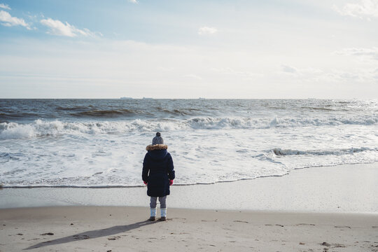 A little girl stands watches the waves at the beach.