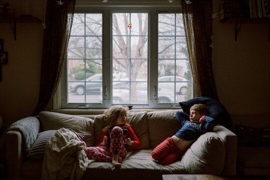 A Boy And A Girl Sit On Their Couch In Pajamas.