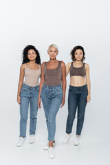 Fototapeta premium Full length of multiethnic women standing near elderly friend on grey background.