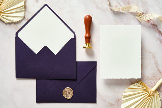 Elegant wedding stationery top view. Flat lay purple envelopes, paper card, dried flowers, wax seal stamp on marble desk.