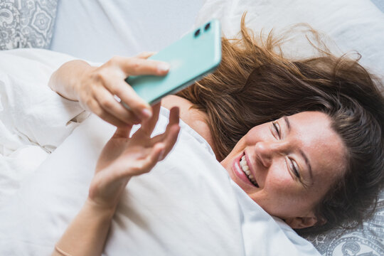 Woman in bed on the phone texting smiling