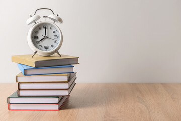 Stack of books and alarm clock on table