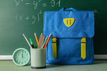 School backpack, holder with stationery and alarm clock on table in classroom