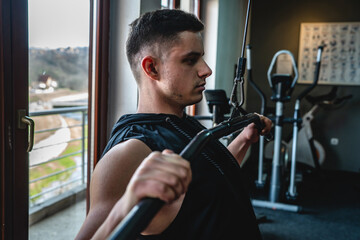 One man young adult caucasian male amateur bodybuilder training back on the cable machine in the gym wearing shirt real people copy space side view