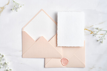 Blank white invitation cards with pink envelopes and gypsophila branches on marble table. Wedding stationery set. Flat lay, top view, copy space.