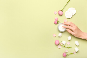 Fototapeta na wymiar Female hand with jar of cosmetic product, cotton balls, pads and rose flowers on green background