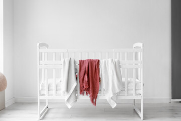 Comfortable crib and soft plaids near light wall