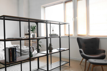 Interior of light bedroom with black bookcase and armchair