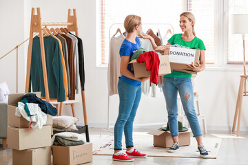 Female volunteers holding boxes with clothes for donation in room