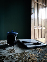 a cup of black coffee and a notebook with a pen on the table with aesthetic light