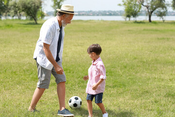 Little boy playing soccer with his grandfather outdoors