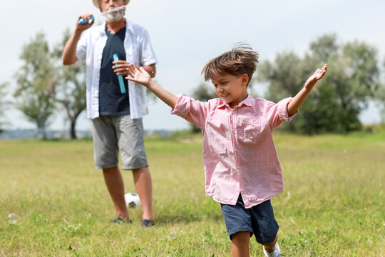 Little boy and his grandfather having fun with soap bubbles outdoors