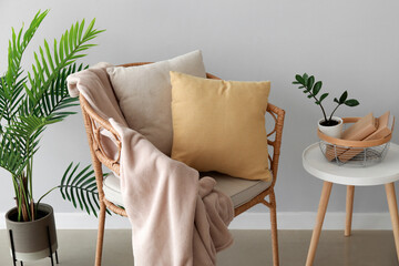 Wicker chair with pillow, plaid and table near light wall