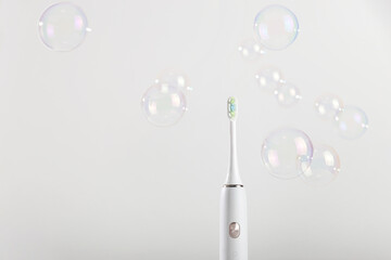 Electronic toothbrush among bubbles on white background.