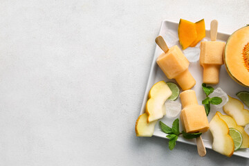 Plate with tasty popsicles and melon pieces on light background